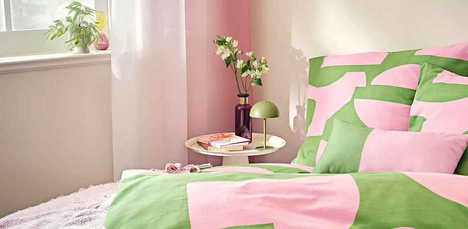 Fris beddengoed in roze en groen brengt een zomerse sfeer in de lichte slaapkamer.