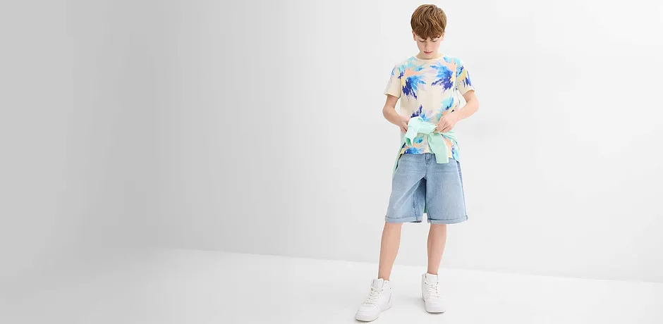 Vrolijk gekleurd overhemd met korte mouwen, T-shirt, lichtblauwe short en witte sneakers.