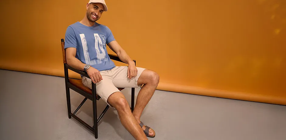 Blauw T-shirt met print, lichte short, pet en sandalen.