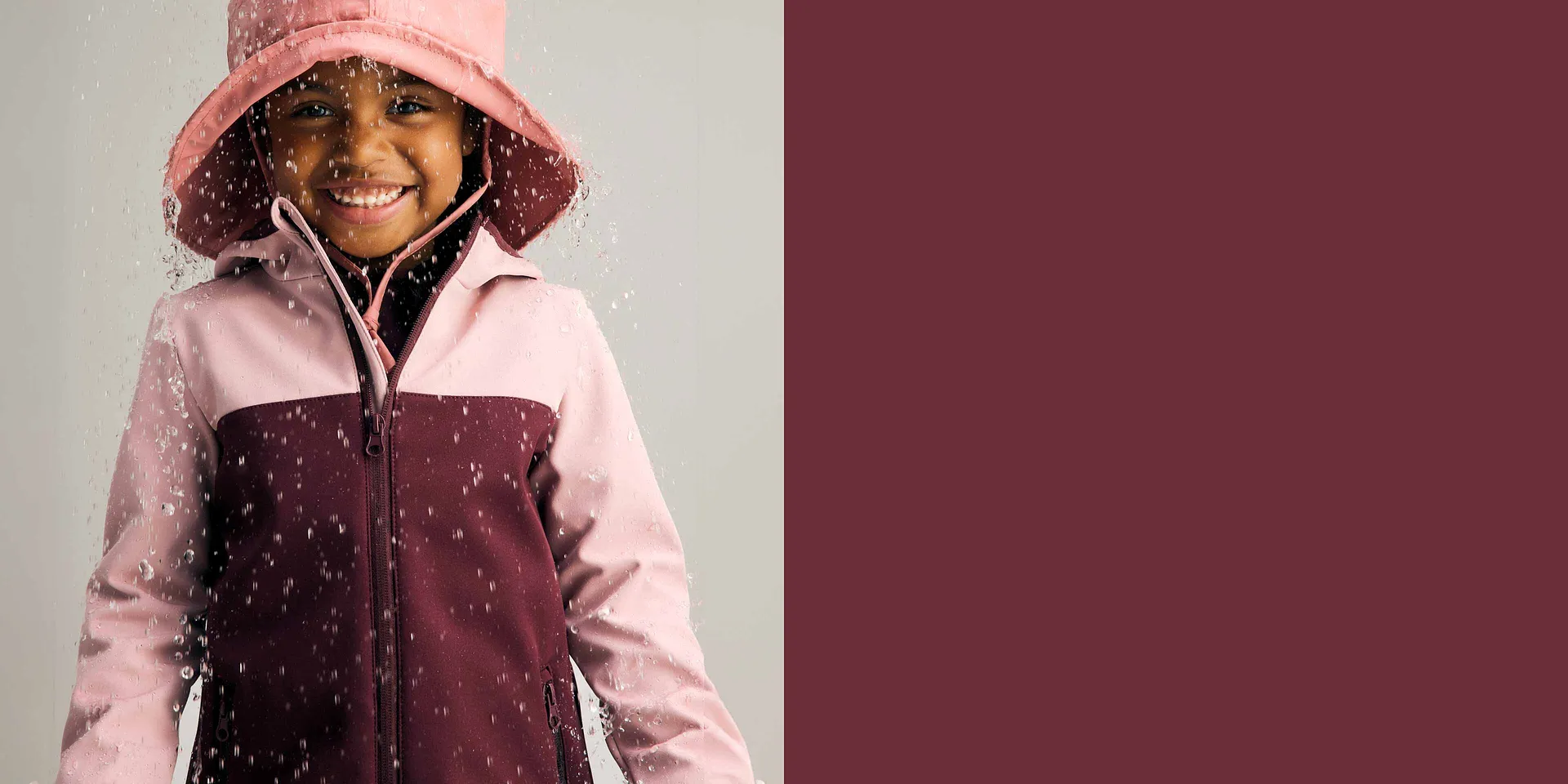 Regenjas in roze en bordeaux gecombineerd met een regenhoed.