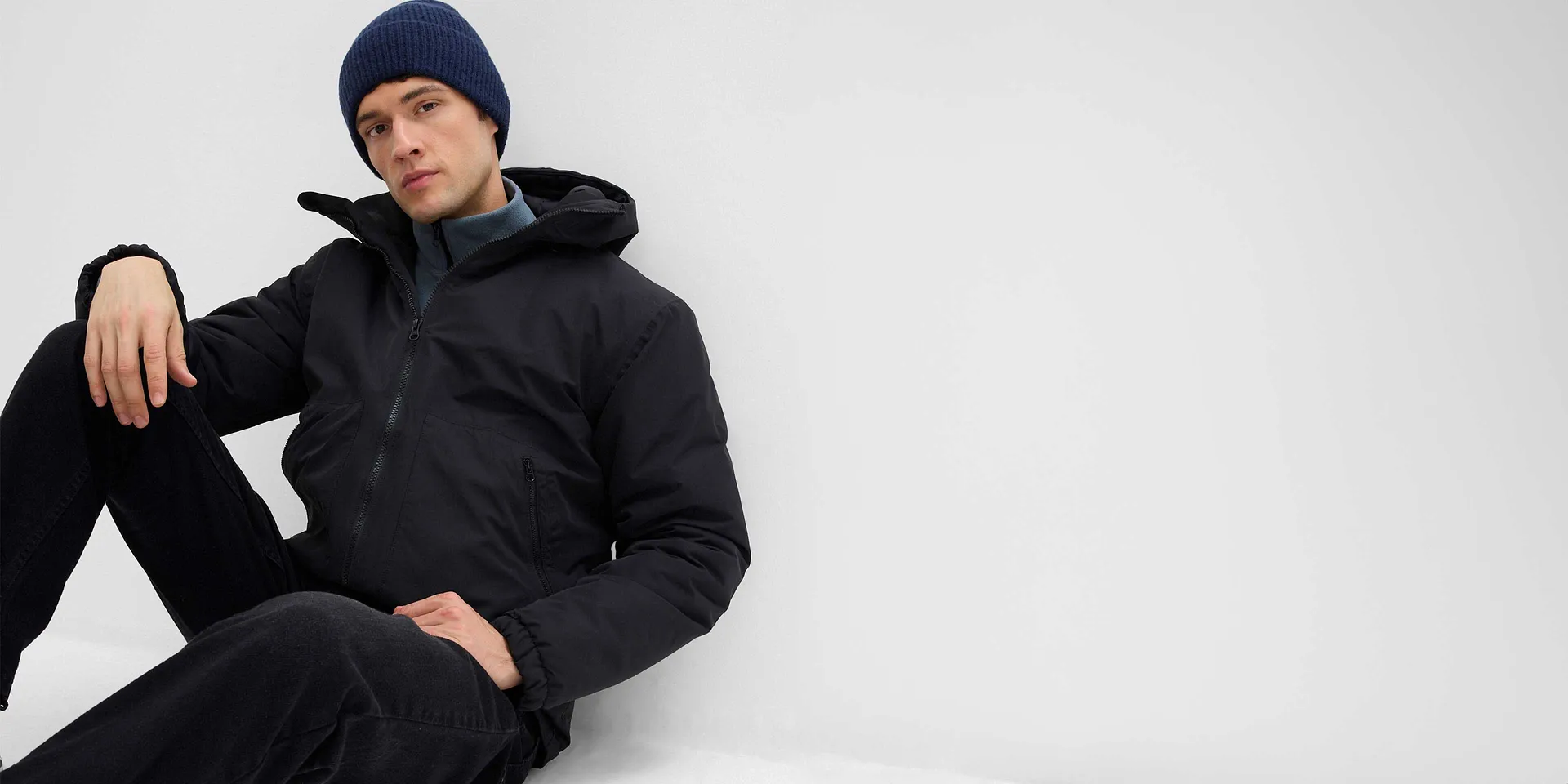 Zwarte winterjas met capuchon, donkerblauwe muts en comfortabele broek voor koude dagen.