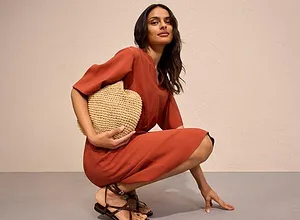 Jumpsuit in roestkleur met korte mouwen, gecombineerd met rieten handtas en fijne sandalen.