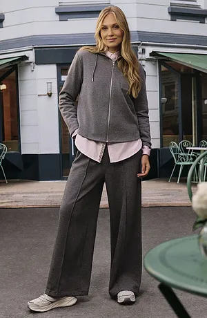 Grijze hoodie over een zachtroze blouse, gecombineerd met een wijde grijze broek en witte sneakers.