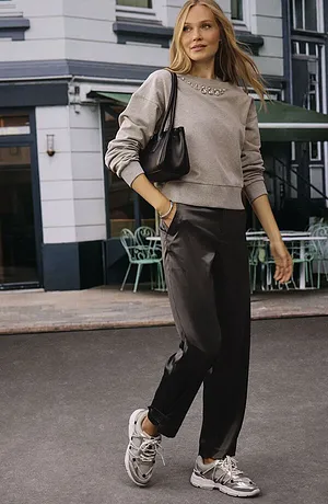 Casual streetstyle: beige trui, donkere broek en witte sneakers. Zwarte handtas als accessoire.