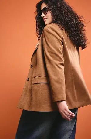 Elegante camelbruine jas met grote knopen, gecombineerd met een donkere rok en een modieuze zonnebril.