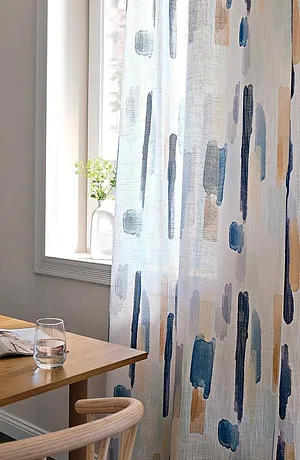 Lichte gordijnen met blauw-grijze penseelstreken sieren het raam en laten zacht licht binnen.