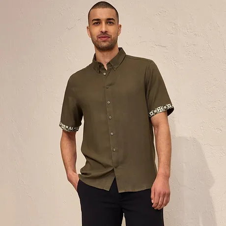 Olijfgroen kortarmshirt met een gedessineerde mouwomslag, donkere shorts en zwarte espadrilles.
