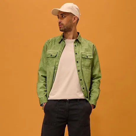Groen overhemd over een wit shirt, donkere short, witte sneakers en een pet.