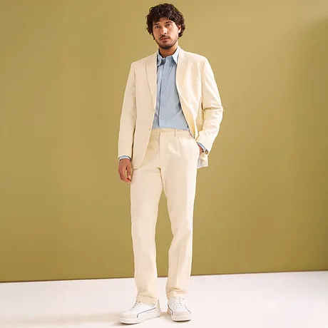 Elegante crèmekleurige pak met lichtblauw overhemd en witte sneakers.