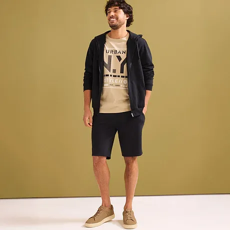 Casual look met beige T-shirt, zwarte hoodie en donkere sweatshorts.