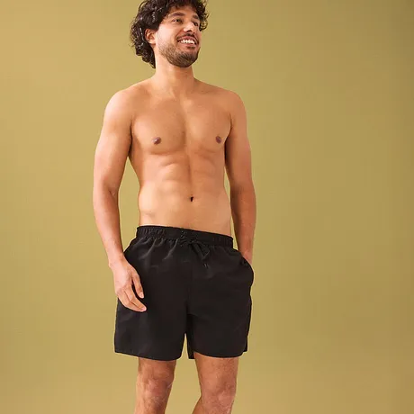 Zwarte badshorts benadrukken de atletische figuur.