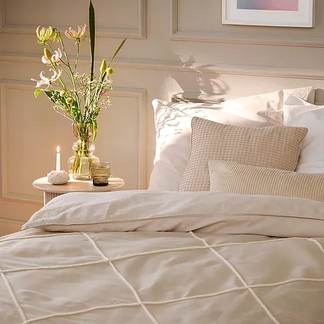 Licht beddengoed met geometrisch patroon siert het bed. Witte kussens en dekens creëren een uitnodigende sfeer.