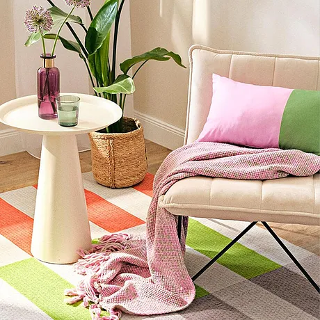 Pastelkleurige textiel in roze en groen siert de zithoek met een deken en kussens.