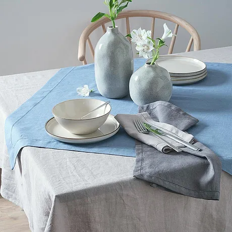 Blauwe en grijze tafelkleedjes versieren de tafel, aangevuld met eenvoudige witte bloemenvaasjes.