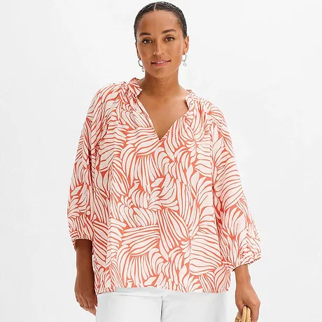 Een luchtige blouse met een oranje palmenpatroon en een witte broek.