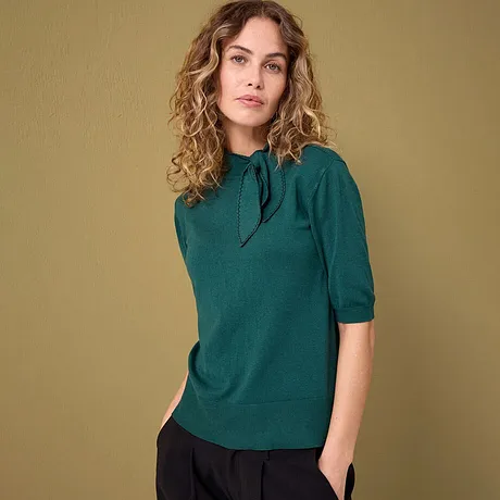 Een elegante smaragdgroene trui met korte mouwen, gecombineerd met een donkere broek.