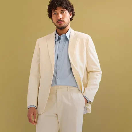 Elegante crèmekleurige pak met lichtblauw overhemd en witte sneakers.
