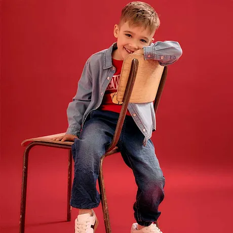 Casual look met een grijze jas, rood T-shirt, spijkerbroek en witte sneakers.