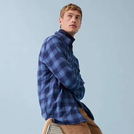 Geruit blauw overhemd, een bruine corduroy broek en witte sneakers.