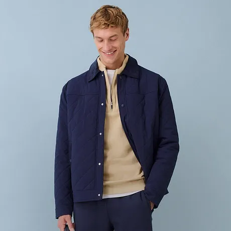 Donkerblauwe jas gecombineerd met een beigekleurige trui en blauwe broek.