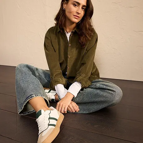 Olijfgroene jas gecombineerd met jeans en witte sneakers met groene biezen.
