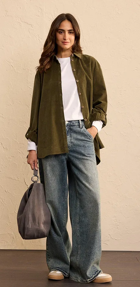 Look met een olijfgroen oversized overhemd, wit T-shirt en wijde spijkerbroek.