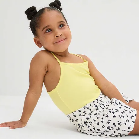 Geel spaghettibandtop en een gebloemde witte rok met zwarte stippen vormen een zomerse outfit.
