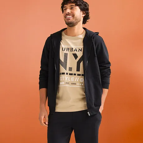 Casual look met beige T-shirt, zwarte hoodie en donkere sweatshorts.
