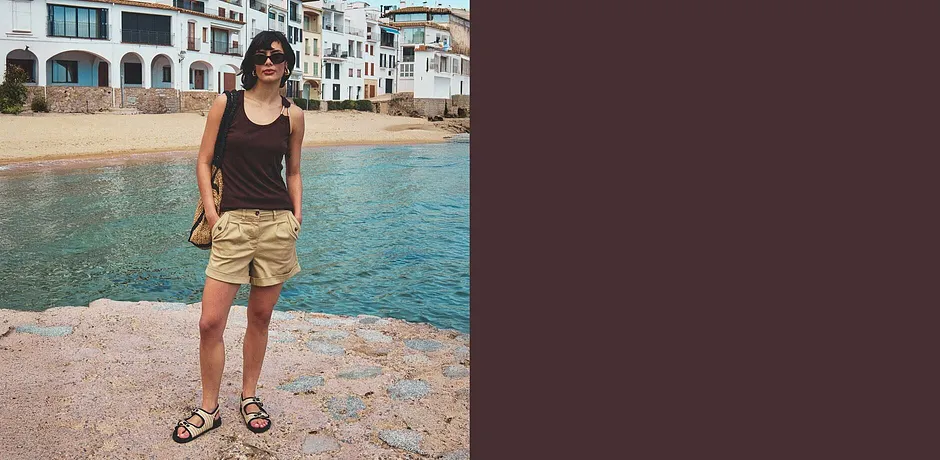 Vrouw draagt een zwart tanktop en beige shorts met sandalen op het strand.