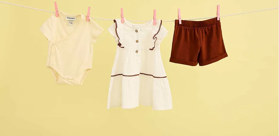 Zomerkleding voor baby's aan de waslijn: romper, witte jurk en bruine shorts voor warme dagen.