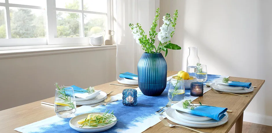 Een blauwe tafelloper siert de eettafel, contrasterend met witte borden en kleurrijke accessoires.