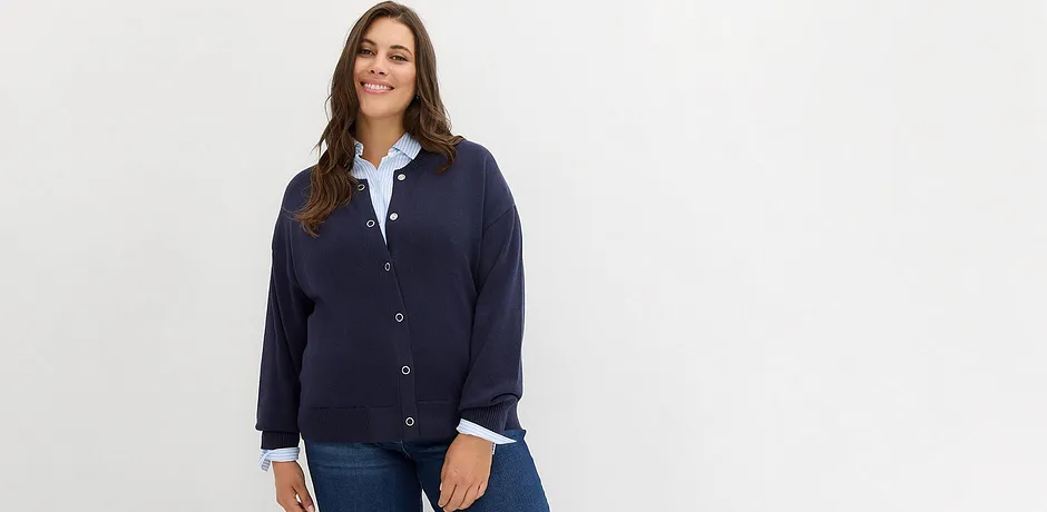 Donkerblauw gebreid vest over een witte blouse, gecombineerd met een klassieke spijkerbroek.