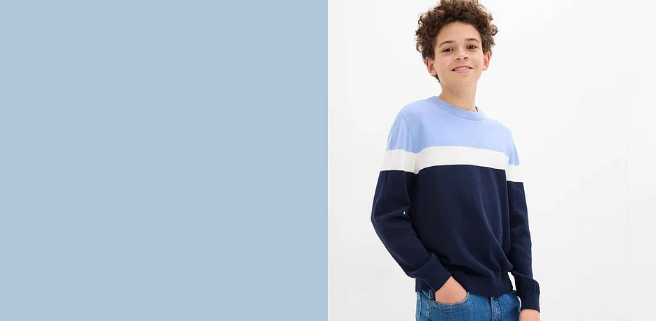 Dreifarbiger Pullover in Blautönen, helle Jeans und eine blaue Baseballkappe vervollständigen den lässigen Look.
