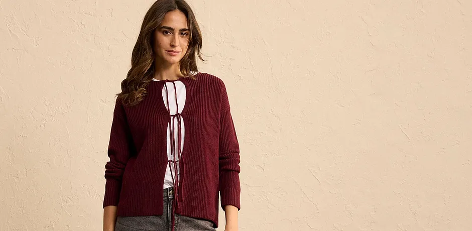 Bordeauxrode gebreide cardigan met strikdetail over een witte blouse.
