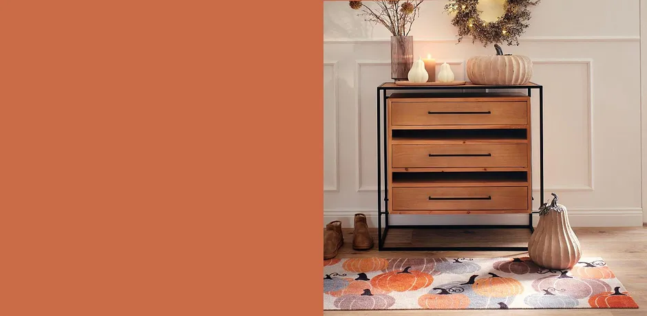Houten ladekast met zwarte grepen, omgeven door herfstdecoraties en warme, aardse kleuren.