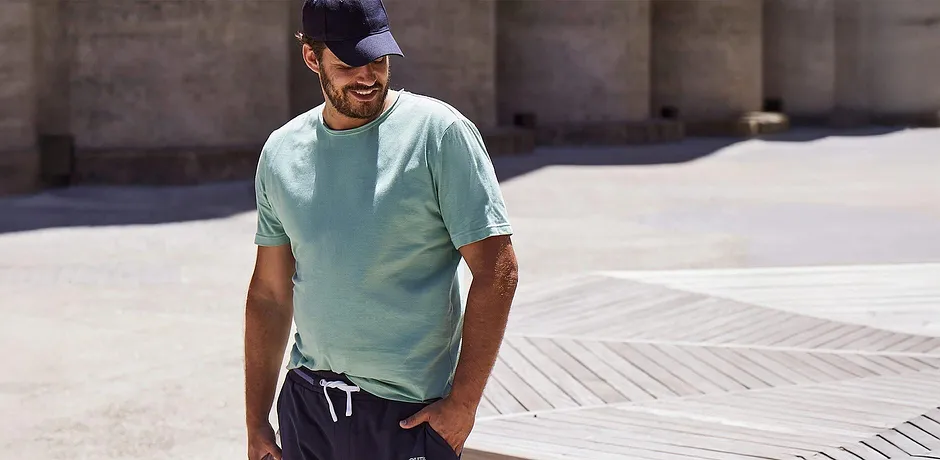 Türkisfarbenes T-Shirt, dunkle Hose & Cap.